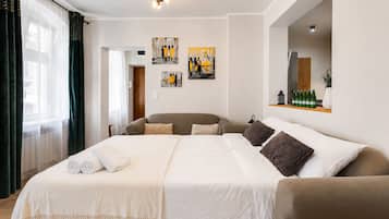 Habitación de hotel con una cama grande, un sofá, un espejo, obras de arte en la pared y una estantería con botellas.