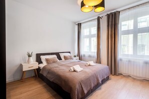 A modern bedroom with a large bed, a bedside table, a nightstand, and a window with curtains. - Aksamitna Przystań przy Starym Rynku (Poznań)