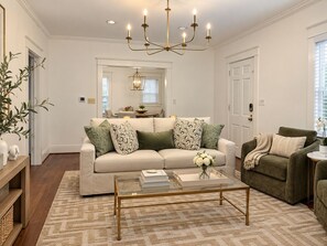 A living room with a beige sofa, a glass coffee table, and a green armchair. - Crimson Cottage | 1.4 Miles to Bryant-Denny! (Tuscaloosa)