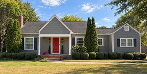 A two-story house with a red front door, a covered porch, and a well-maintained lawn. - Crimson Cottage | 1.4 Miles to Bryant-Denny! (Tuscaloosa)