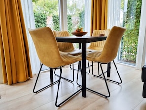 Ein Essbereich mit Tisch und Stühlen, einer Obstschale und Blick auf Grünflächen.