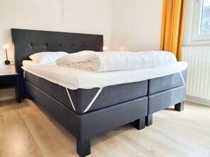 Ein modernes Schlafzimmer mit einem dunkelgrauen Bett, weißer Bettwäsche und einer Nachttischlampe.