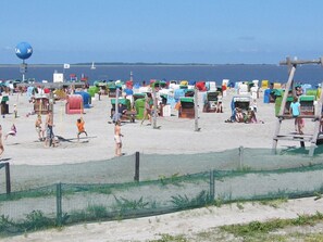 A beach with multiple colorful beach huts and a netted area in the foreground. - Holiday Home in Dornum With Barbecue (Dornum)