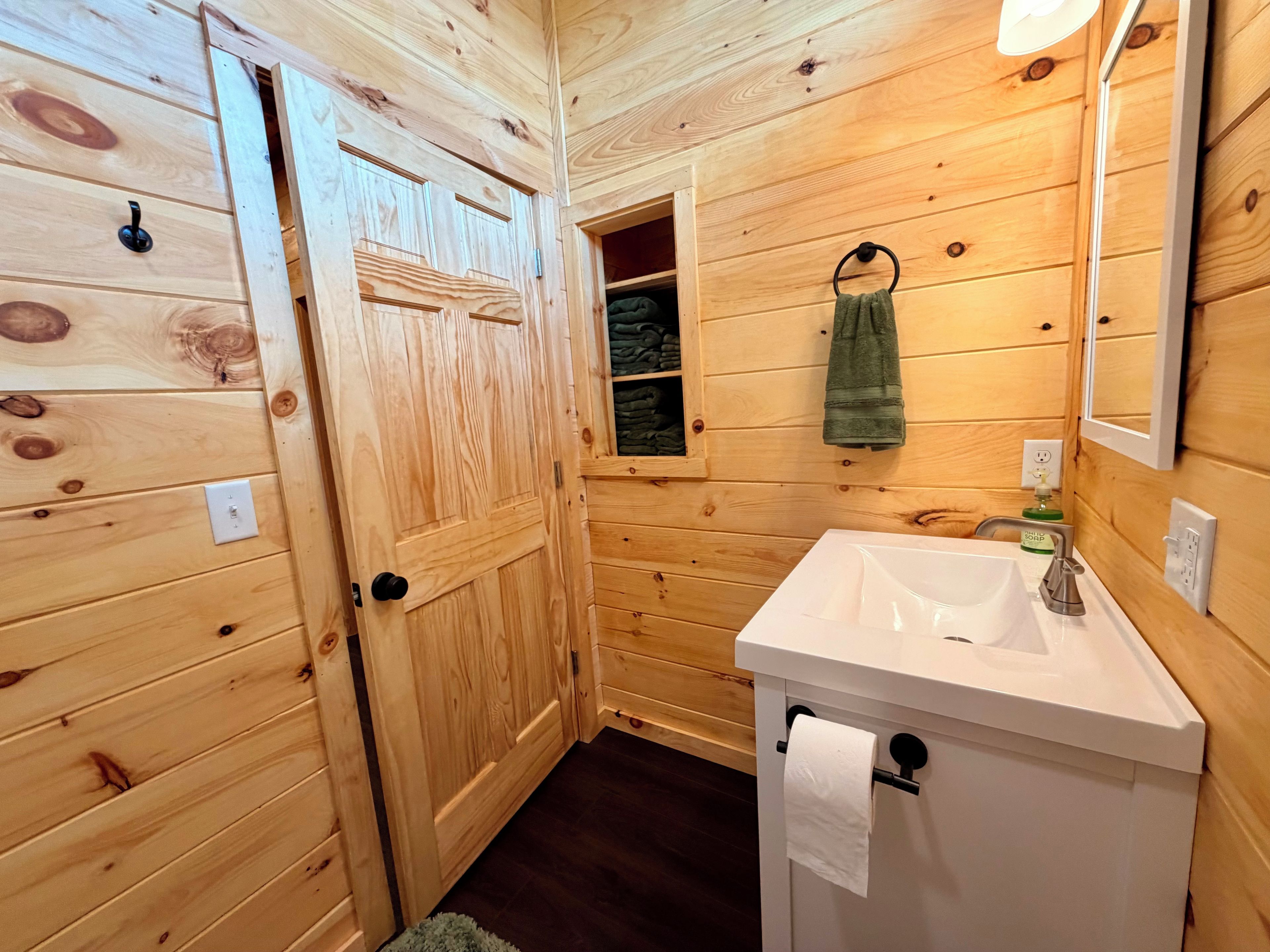 A wooden cabin bathroom with a white sink, a towel hanging on the wall, and a small window.