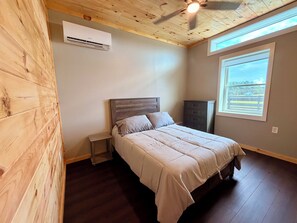 Ein Schlafzimmer mit einem Bett, einem Nachttisch, einer Klimaanlage, einem Fenster mit Aussicht und einem Deckenventilator.
