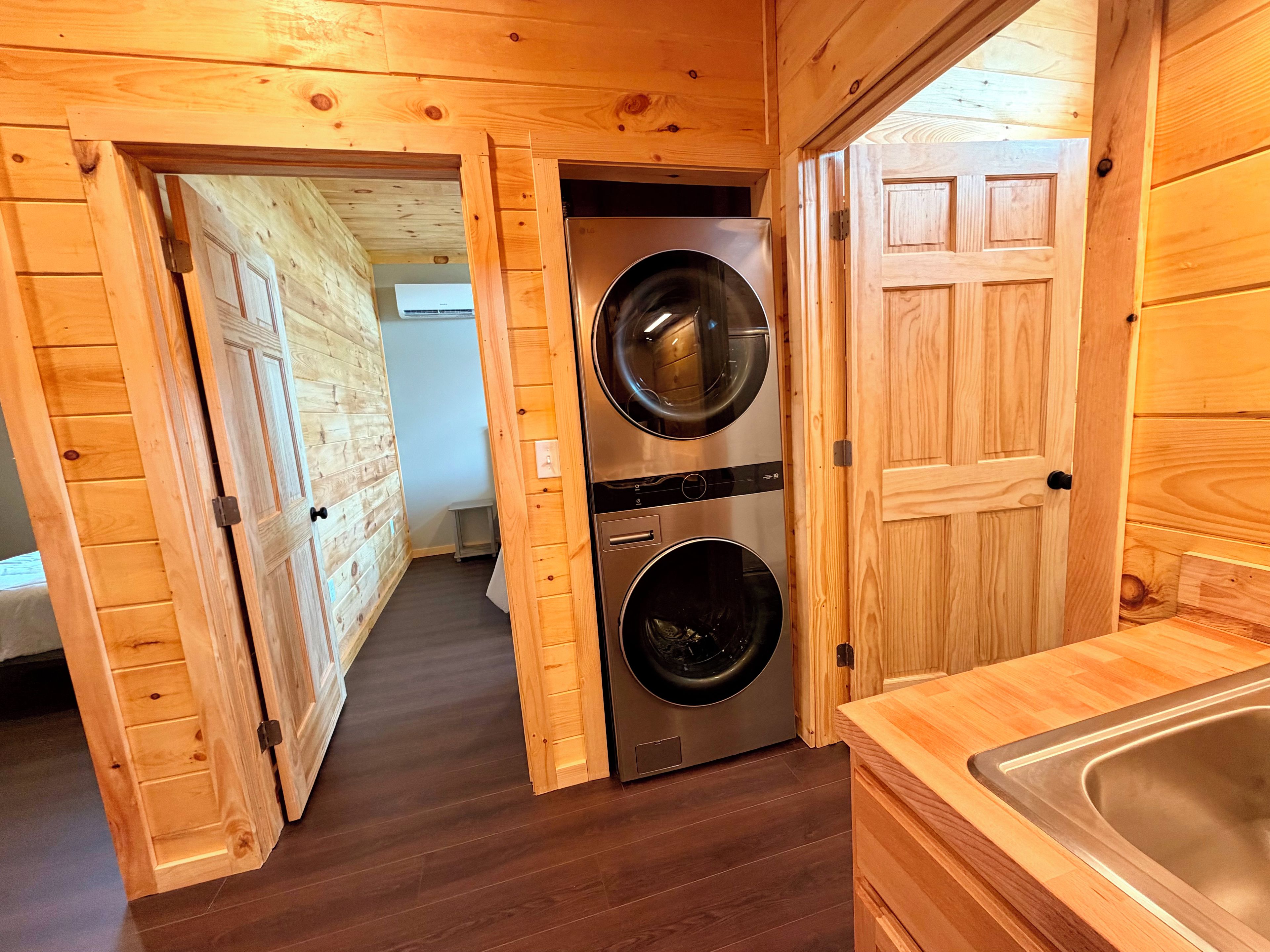 A laundry room with two stacked washing machines, wooden walls, and a wooden floor.