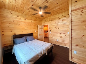 Een kamer met houten lambrisering, een bed, een plafondventilator en uitzicht op een keuken.
