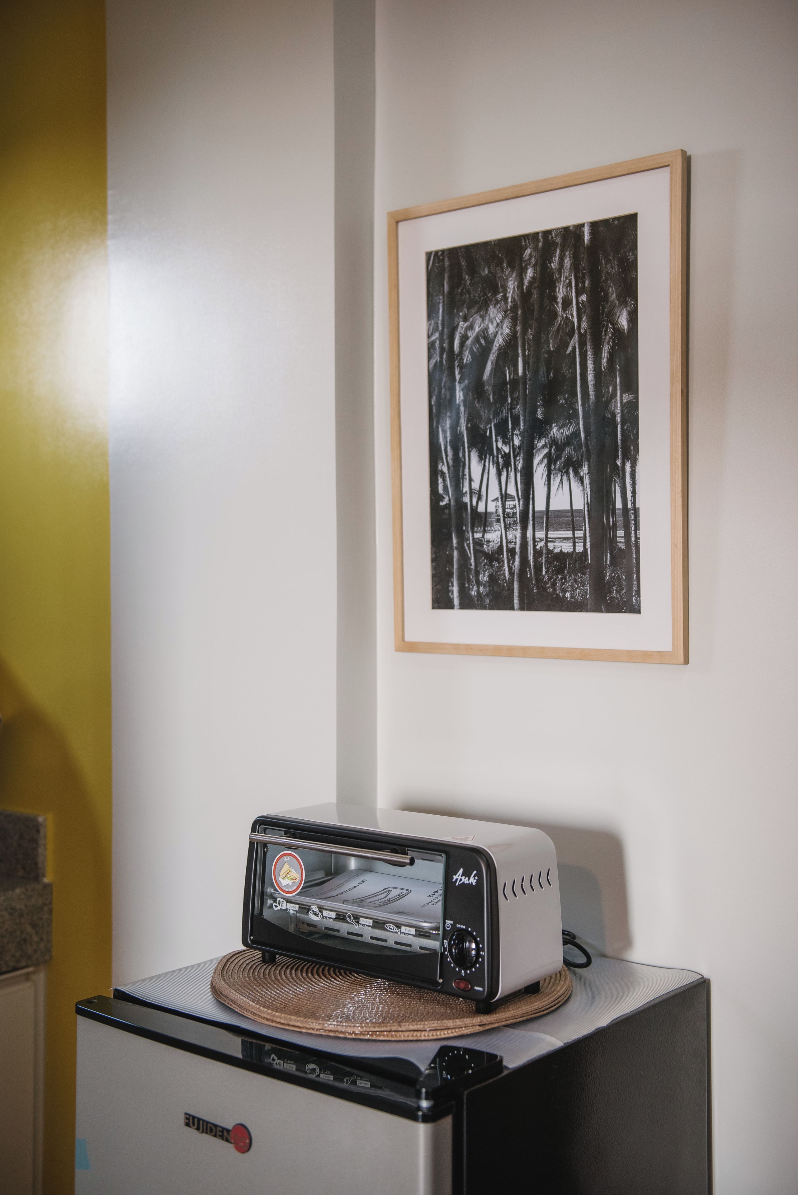 A kitchen area with a toaster on a stand, a framed black and white photograph on the wall, and a yellow wall.