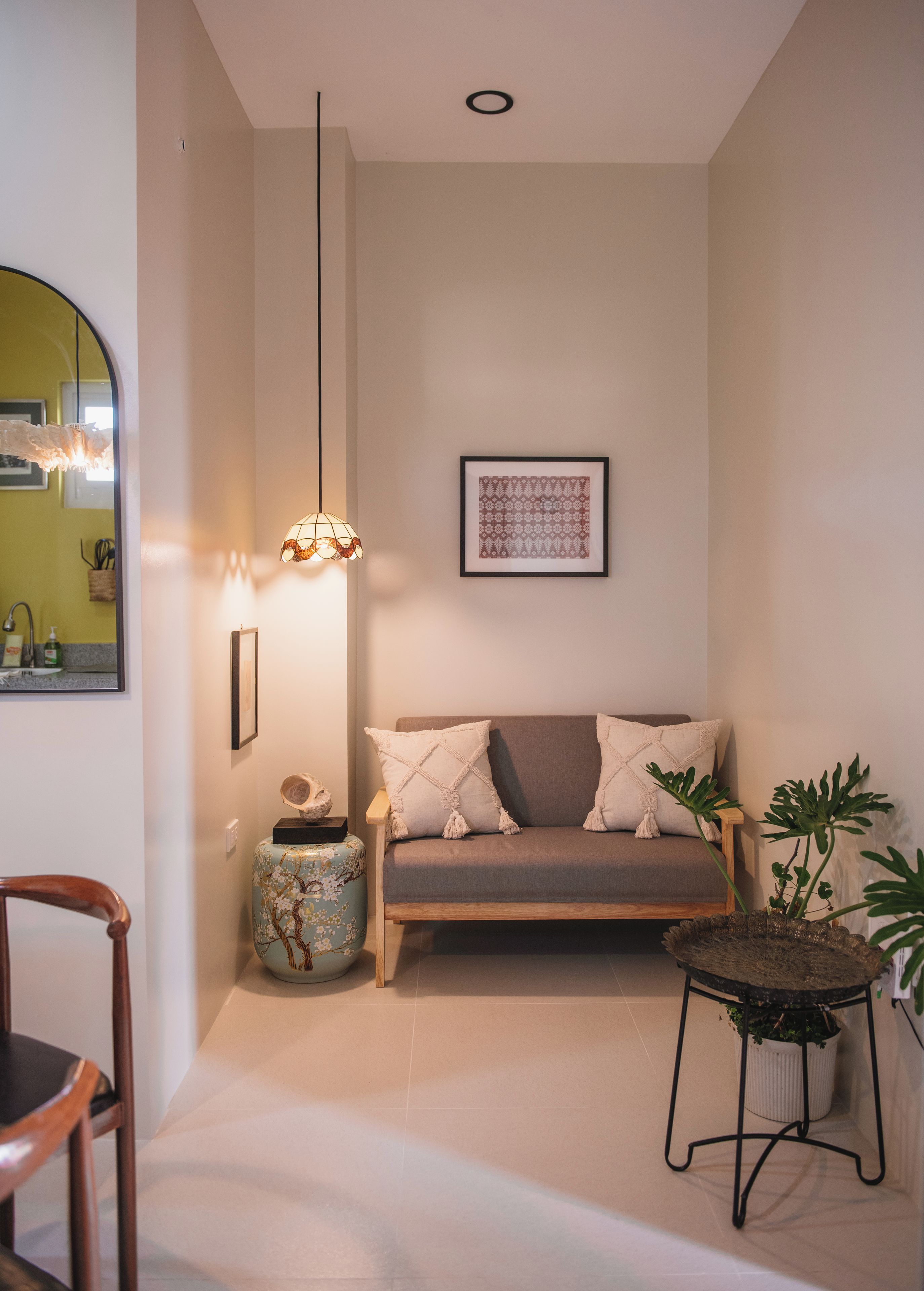 A cozy living room with a sofa, a wooden chair, a small table with a plant, and a hanging light fixture.