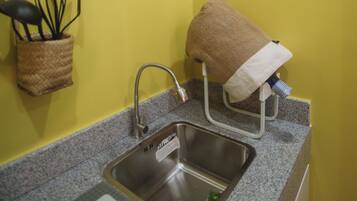 A kitchen with a stainless steel sink, a window, and a framed picture on the wall.