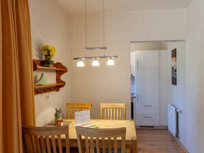 A dining area with a wooden table, chairs, a hanging light fixture, and a kitchen in the background. - Holiday Apartment With 1 Bedroom (Braunlage)