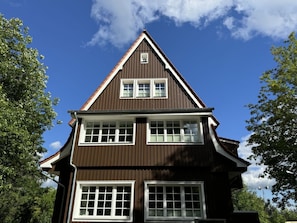 Ein zweistöckiges Haus mit einem steilen Satteldach, zahlreichen Fenstern und einem sichtbaren Schornstein.