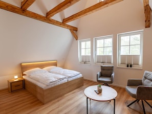 Ein Schlafzimmer mit einem hölzernen Bett, einem Nachttisch mit Lampe, einem runden Tisch mit Fernbedienung und zwei Stühlen.