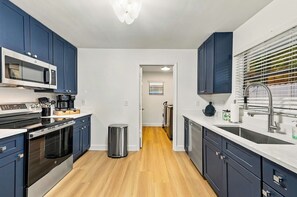 A modern kitchen with dark blue cabinets, a stainless steel range, a microwave, and a sink with a modern faucet. - Palm Beach Retreat | Pool, Cold Plunge & Games (West Palm Beach)