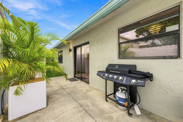 Un patio con una griglia barbecue, un vaso bianco con palme e una casa con porta scorrevole in vetro.