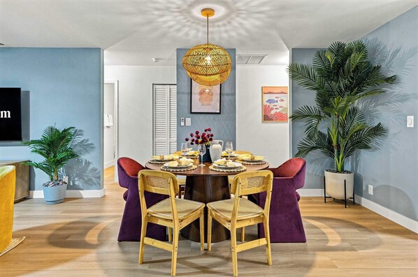 A dining area with a round table, four chairs, a hanging light fixture, and wall art. - Palm Beach Retreat | Pool, Cold Plunge & Games (West Palm Beach)