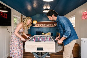 A room with a foosball table, a TV displaying 'FLIX', and a neon sign reading 'PAL PLA'. - Palm Beach Retreat | Pool, Cold Plunge & Games (West Palm Beach)