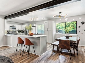 A modern kitchen with white cabinets, a central island, and a dining area with a table and chairs. - Jungle Oasis - Pool + Hot Tub + Game Rooms (Richardson)