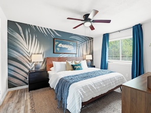 A bedroom with a bed, nightstands, a ceiling fan, a window with curtains, and a wall with a leaf pattern. - Jungle Oasis - Pool + Hot Tub + Game Rooms (Richardson)