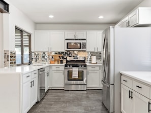 A modern kitchen with white cabinets, stainless steel appliances, and a tiled backsplash. - Jungle Oasis - Pool + Hot Tub + Game Rooms (Richardson)