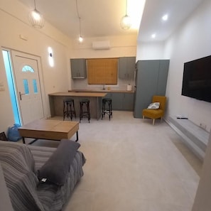 A compact living space with a kitchenette, a sofa, a dining area, and a TV mounted on the wall. - Yard House 284 Kalamata (Kalamata)