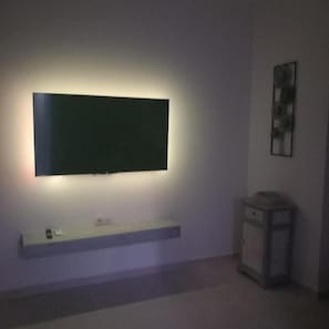 A room with a mounted flat-screen TV on the wall, a small shelf below it, and a cabinet to the right. - Yard House 284 Kalamata (Kalamata)