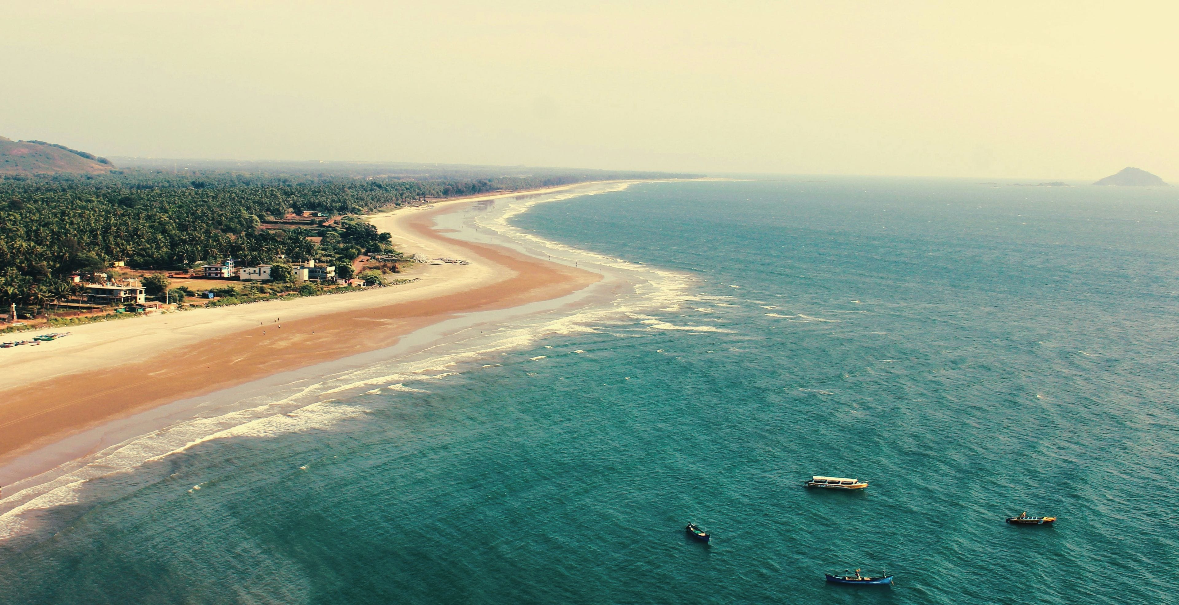 Paisagem costeira com praia, oceano e alguns barcos.