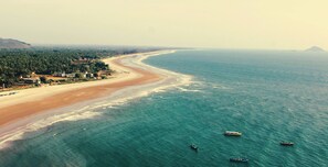 A coastal landscape with a beach, ocean, and a few boats.