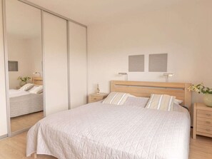 A bedroom with a bed, nightstands, a mirror, and a sliding door. - Holiday Apartment in Groote Keeten With Wi-fi (Callantsoog)