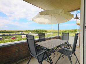 A balcony with a table and chairs, an umbrella, and a view of a highway and greenery. - Holiday Apartment in Groote Keeten With Wi-fi (Callantsoog)