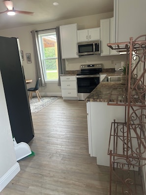 A kitchen with white cabinets, a microwave, an oven, and a sink.