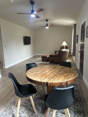Un comedor con una mesa redonda de madera, sillas negras, un ventilador de techo y un televisor montado en la pared.