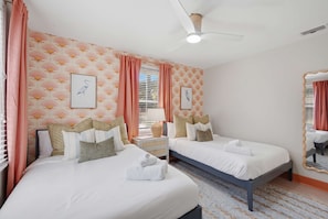 Ein Hotelzimmer mit zwei Betten, einem Deckenventilator, einem Fenster mit Jalousien und einem Spiegel an der Wand.