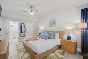Een slaapkamer met een bed, nachtkastjes, een plafondventilator, een inlijsting afbeelding aan de muur, en een deur naar de badkamer.