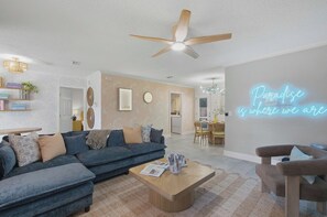 Ein modernes Wohnzimmer mit einem blauen Sofa, einem Holztisch und einem Neonzeichen an der Wand.