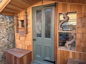 Eine Holztür mit einem grünen und einem Glasfeld, eine Steinwand und eine kleine Holzbank.
