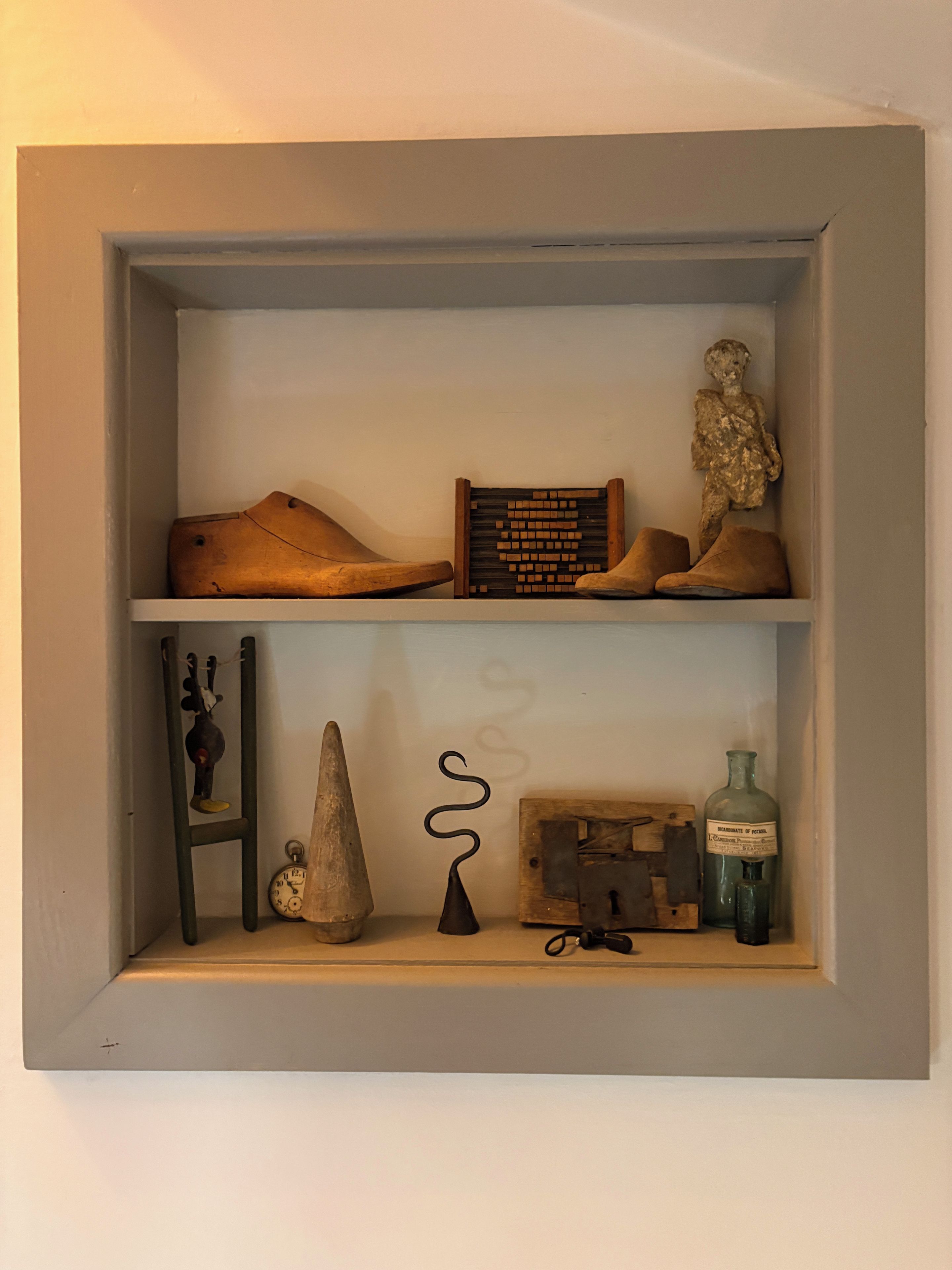 A shelf with various items including a wooden object, a figurine, a clock, and bottles.