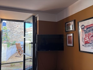 Ein Zimmer mit Fernseher, einer Tür zu einem Außenbereich und einer Wand mit gerahmten Bildern.