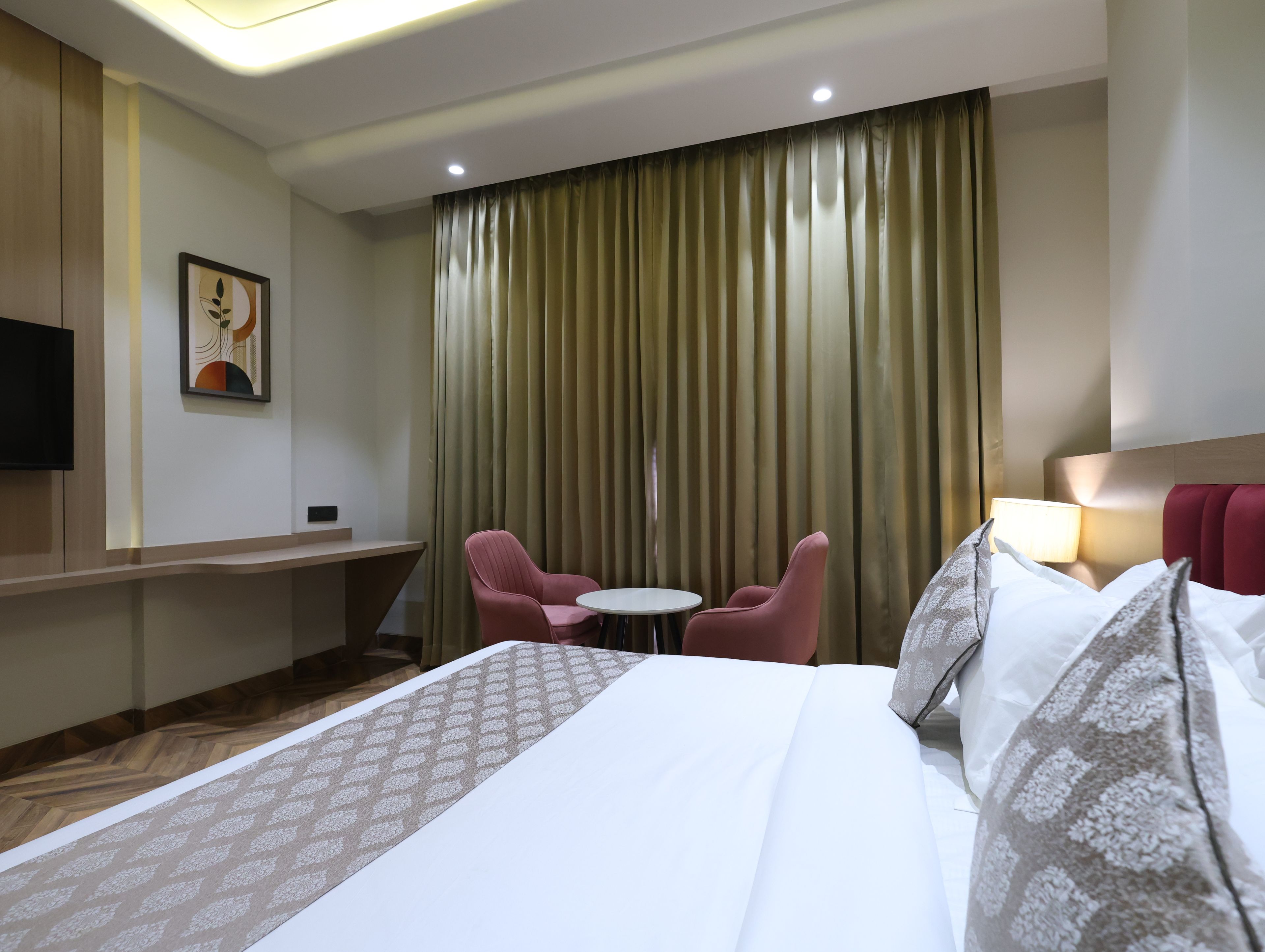 A hotel room with a bed, two chairs, a small table, a TV, and a curtain.