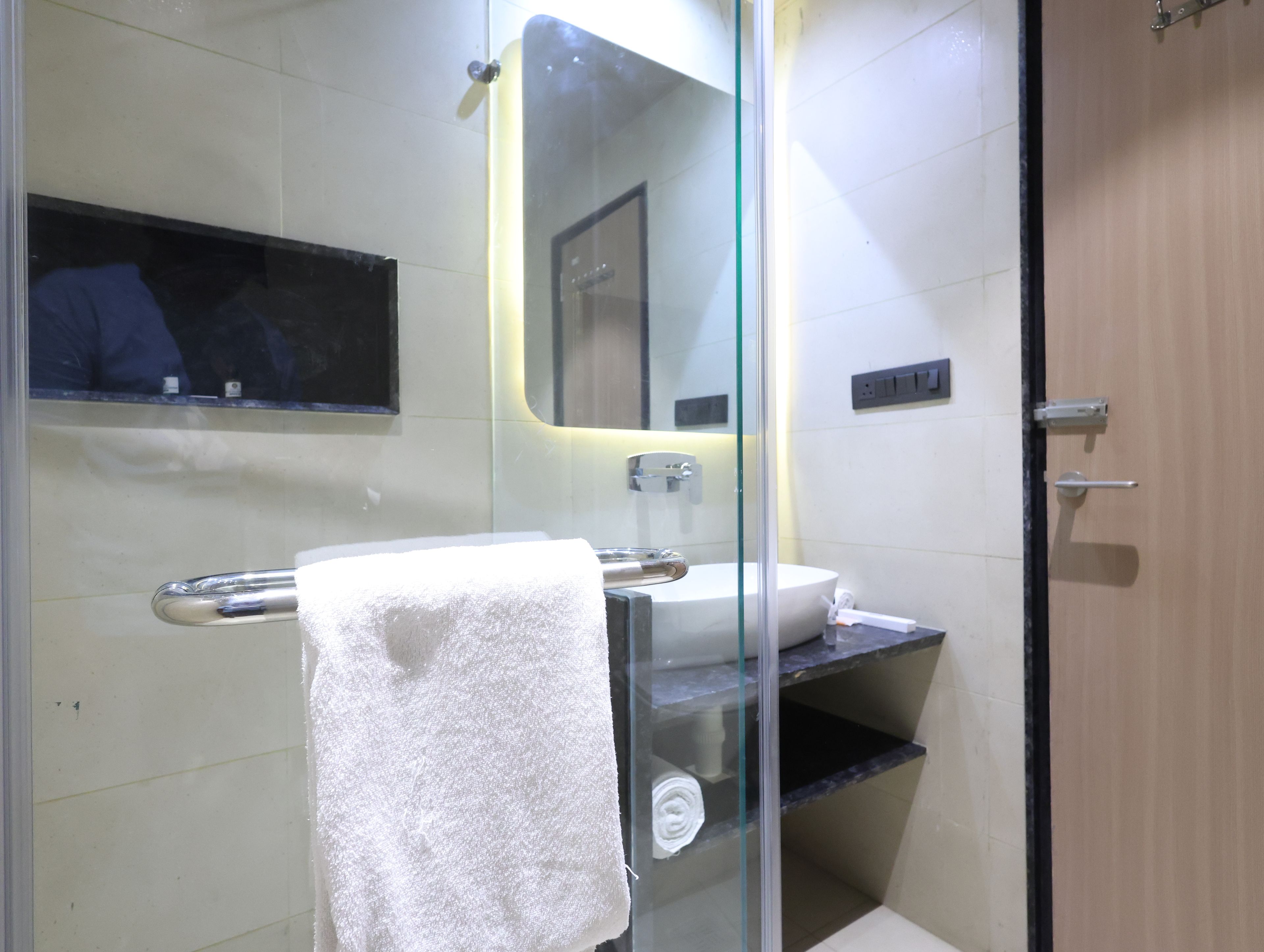 Un baño moderno con cabina de ducha de vidrio, un lavamanos blanco y una toalla colgada en un perchero.