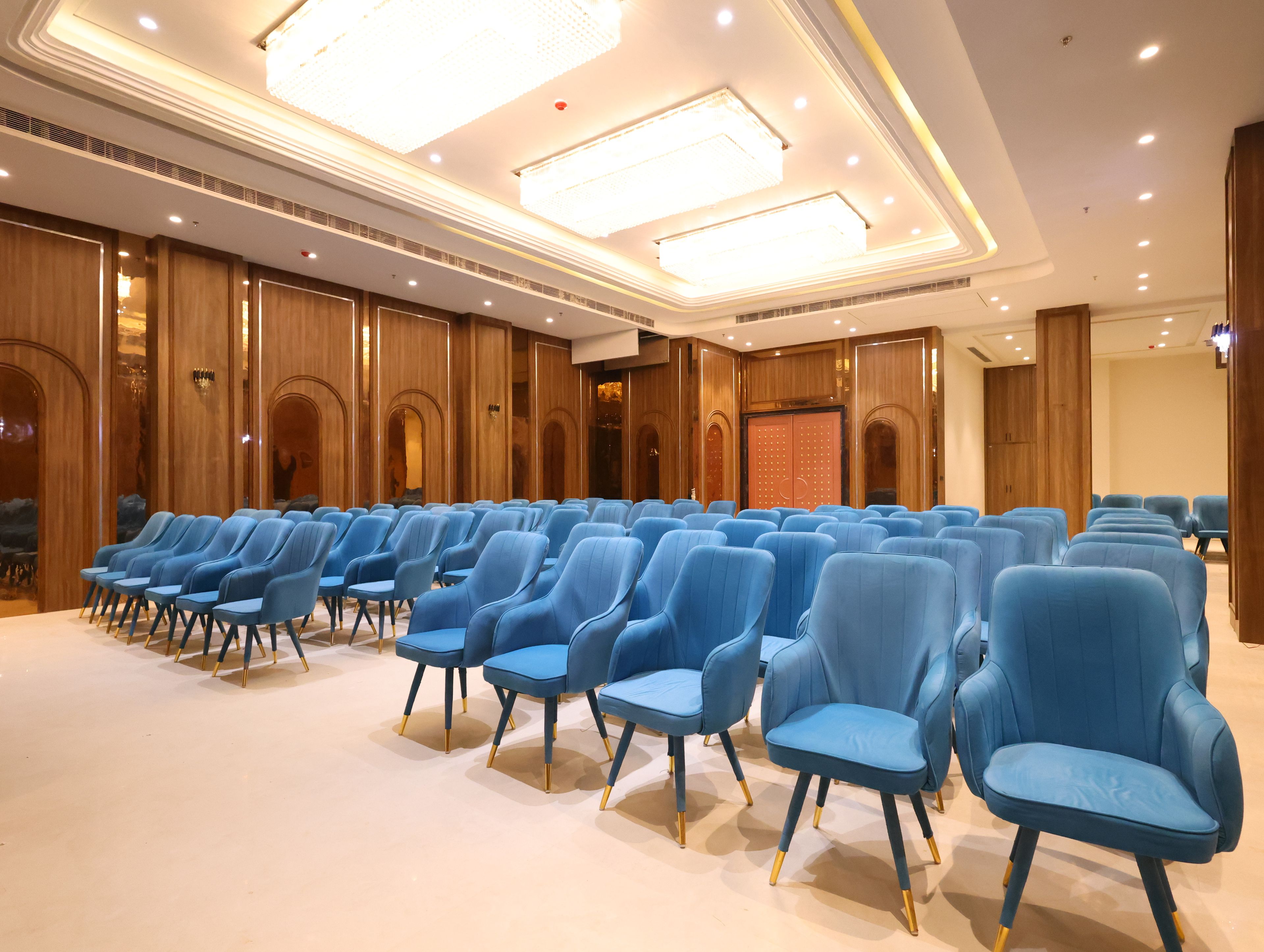 A conference room with rows of blue chairs, wooden paneling, and recessed ceiling lighting.