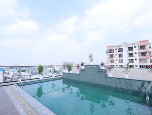 Una piscina en la azotea con borde de azulejos, rodeada de plantas en macetas y vistas a un paisaje urbano.