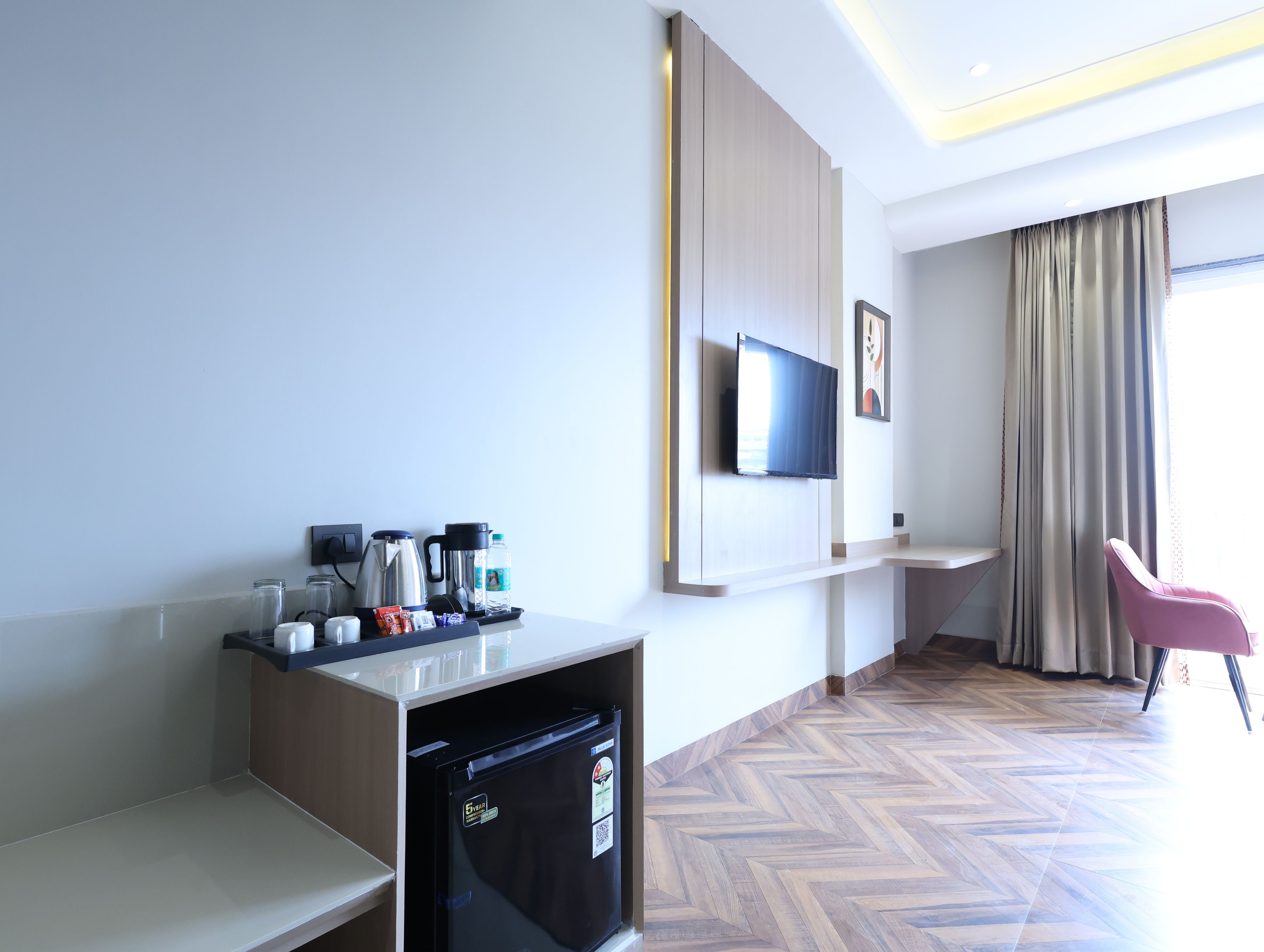 A hotel room with a kitchenette, a flat-screen TV, a seating area, and a herringbone-patterned floor.