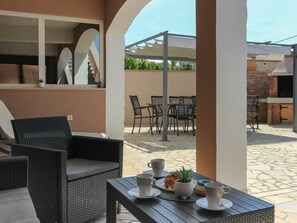 An outdoor seating area with wicker furniture, a table with cups and a plant, and a view of a building with a staircase. - Dvori With Private Pool (Liznjan)