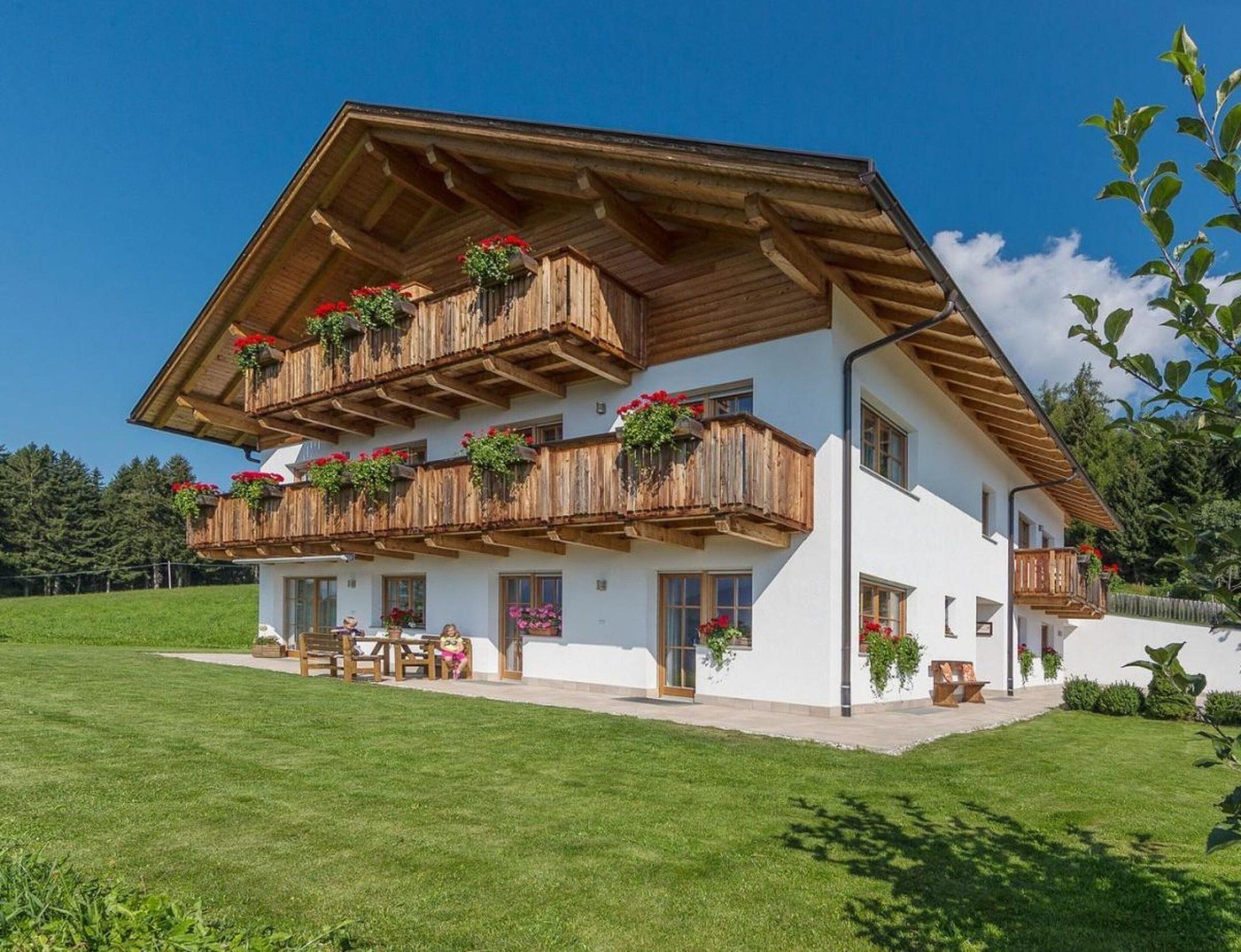 A two-story chalet with wooden balconies, a covered patio, and a well-maintained lawn.