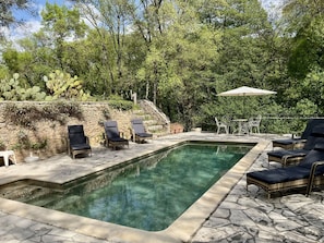 A swimming pool with lounge chairs and a table, surrounded by greenery and a stone wall. - Holiday Home With 1 Bedroom (Entrecasteaux)