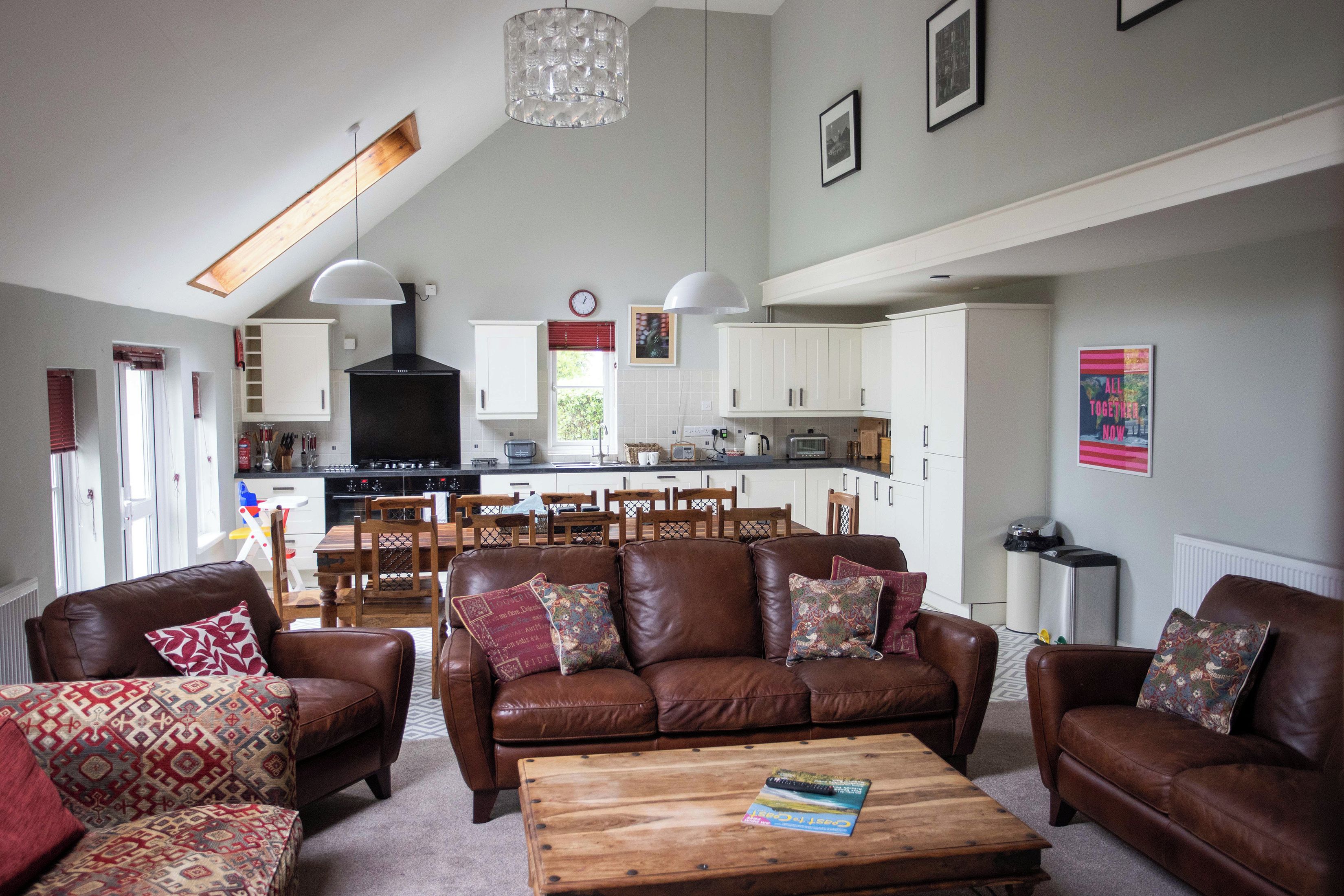 A spacious living room with a brown leather sofa set, a wooden coffee table, and a dining area with a wooden table and chairs.