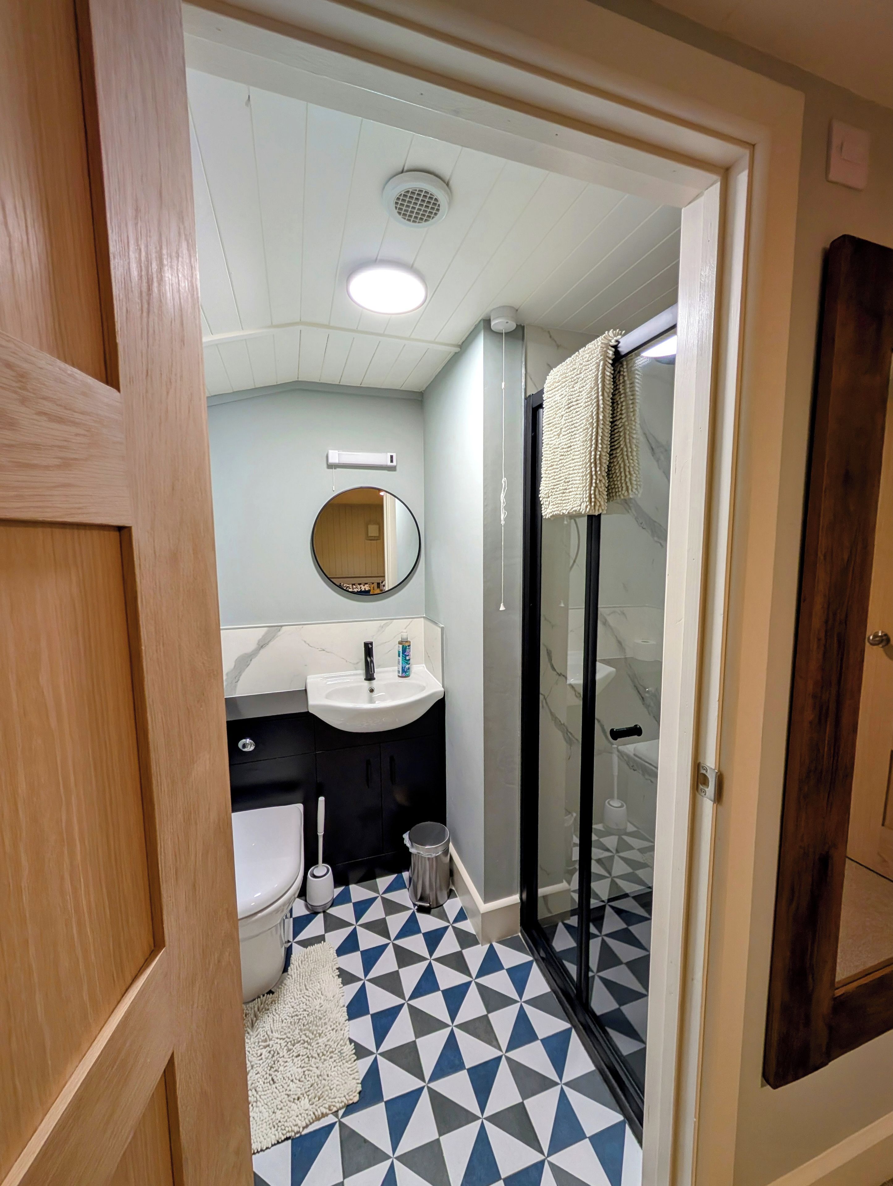 Un baño con lavamanos blanco, un espejo redondo, inodoro y zona de ducha con puerta de cristal.