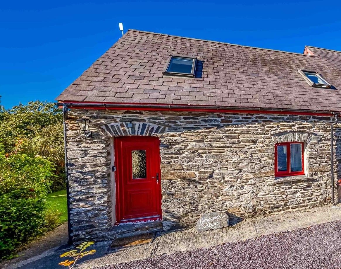 A stone cottage with a red door, two small windows, and a chimney.