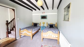 Une pièce avec deux lits en bois, un tapis à motifs, un plafond avec des poutres apparentes et un luminaire suspendu.